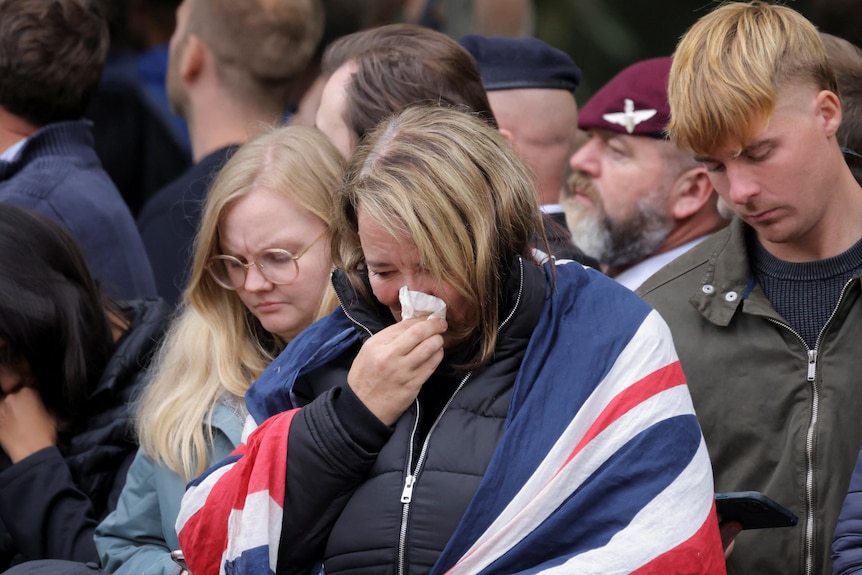 A woman has a Union Jack draped over he shoulders and a tissue held to her nose. 