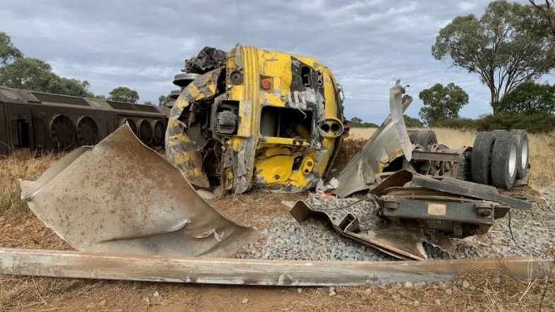 A bright-coloured diesel locomotive on its side after a collision with a truck in the countryside.