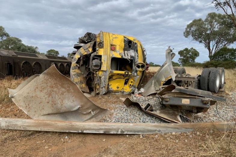 A bright-coloured diesel locomotive on its side after a collision with a truck in the countryside.