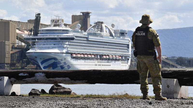A man in army uniform on a shoreline looking at a cruise ship.
