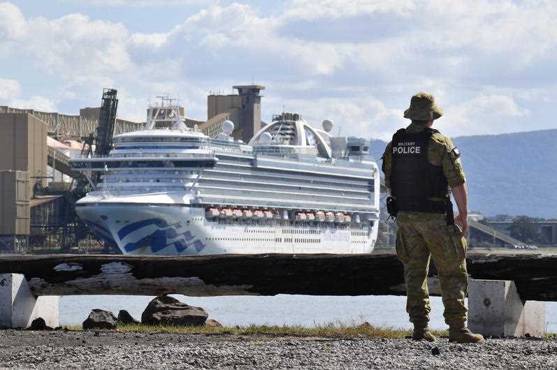A man in army uniform on a shoreline looking at a cruise ship.