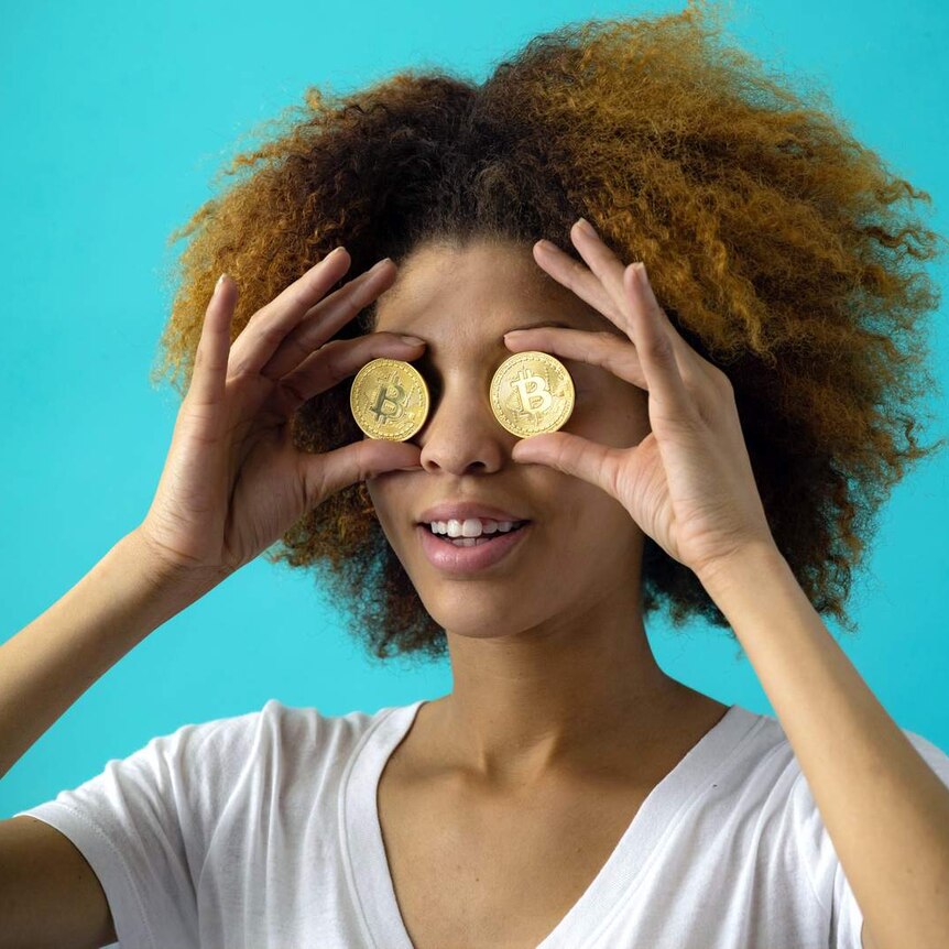 Young woman is holding two bitcoins over her eyes.