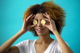 Young woman is holding two bitcoins over her eyes.