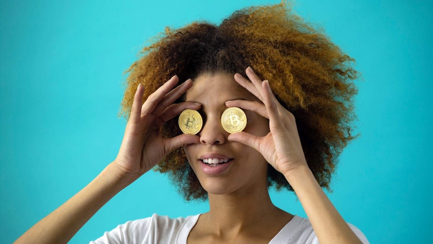 Young woman is holding two bitcoins over her eyes.