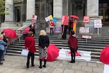 People with protest signs on steps of Parliament House