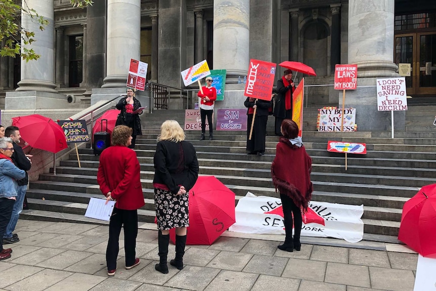 People with protest signs on steps of Parliament House