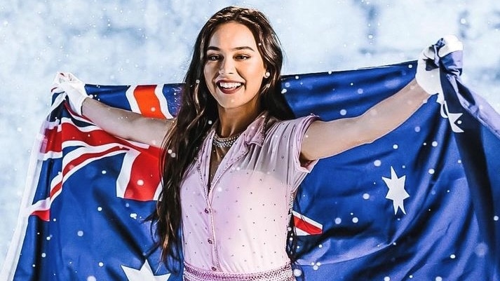 A young woman wearing a pink sparkly dress holding up an Australian flag behind her.