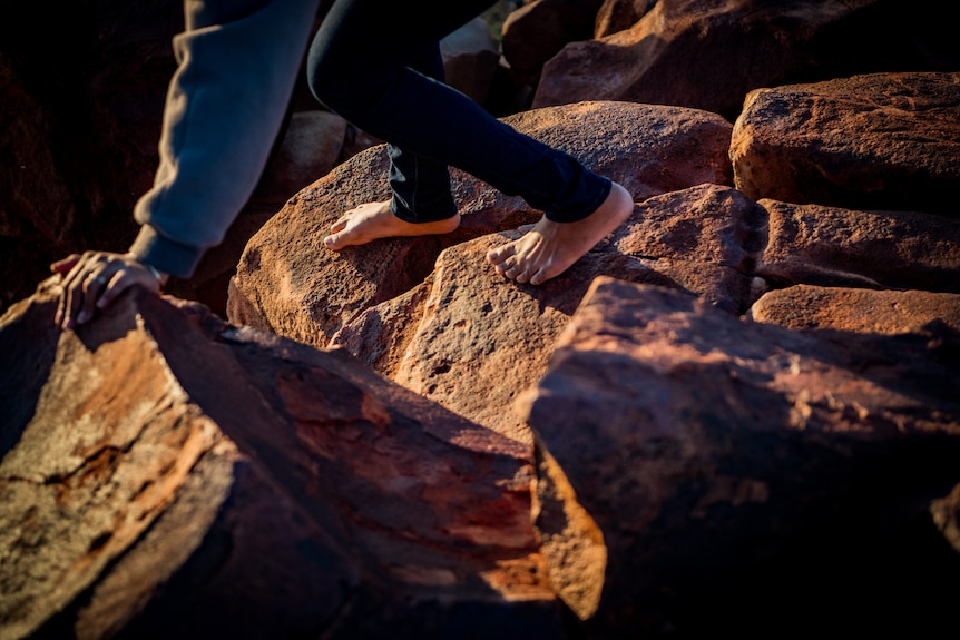 Raelene Cooper, bare-footed, has one hand on the rocks as she climbs over them.