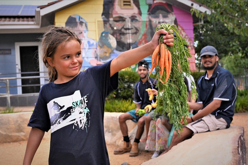 A girl holds up a bunch of carrots