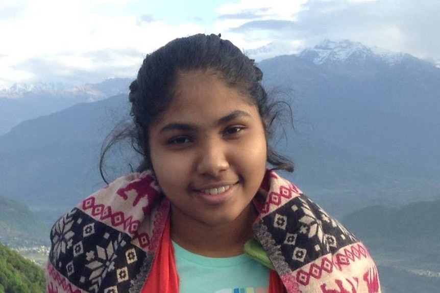 Nisali Perera smiles at the camera in front of a view of a mountain.