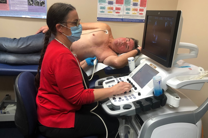 A man lies down while a woman conducts a check on his heart and looks at the results on a screen