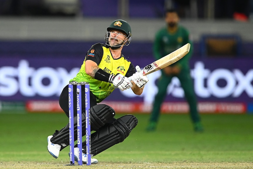 An Australian batsman looks behind him to watch the ball go over the fence after a ramp shot.