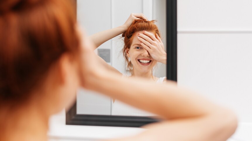 Woman standing in a bathroom smiling in mirror reflection