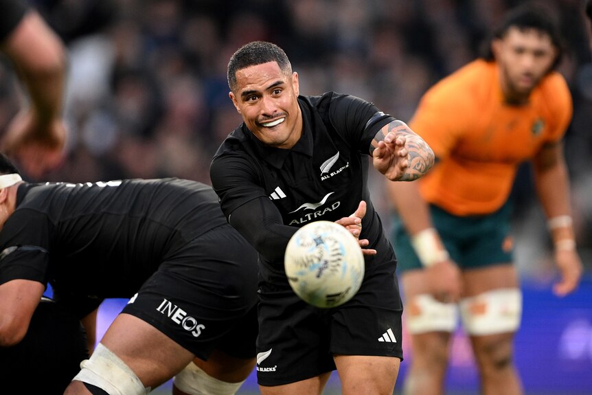 An All Blacks player passes the ball to his left against the Wallabies.