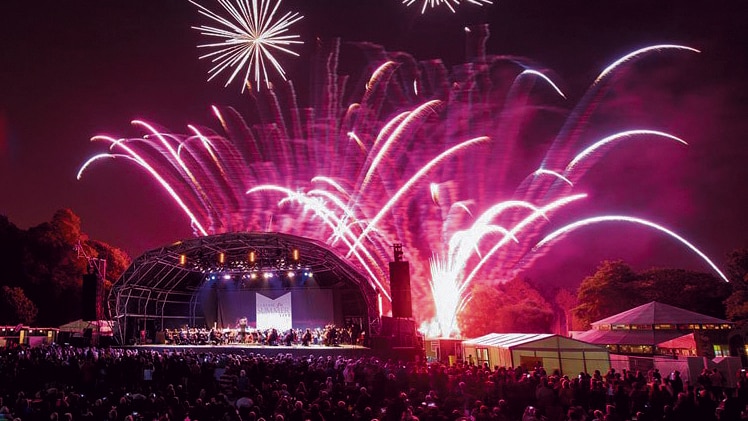 Fireworks light up the sky above a stage filled with a symphony orchestra
