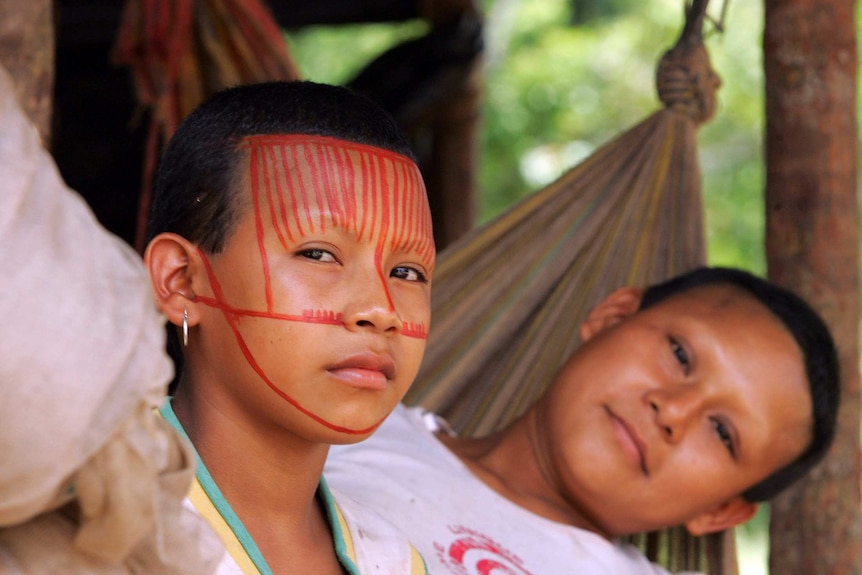 Two women in a hammock. One has red painted marking on her face.