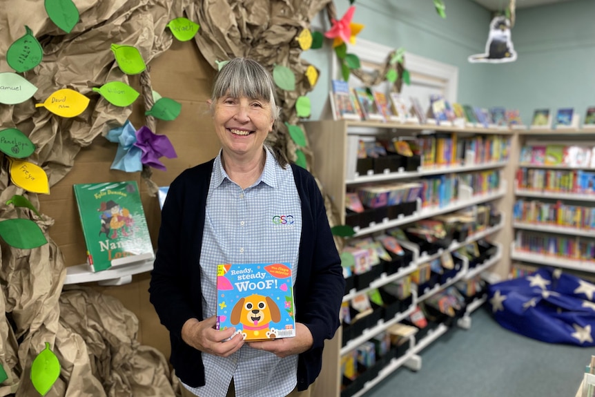 A woman holds a children's book in a library.