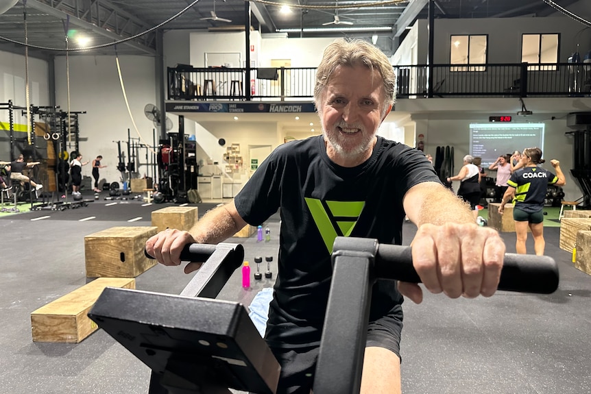 Chris sitting on an exercise bike, hands on the handles, smiling.