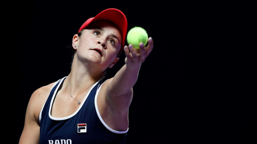 Ash Barty about to toss the ball up to serve, with a dark background.