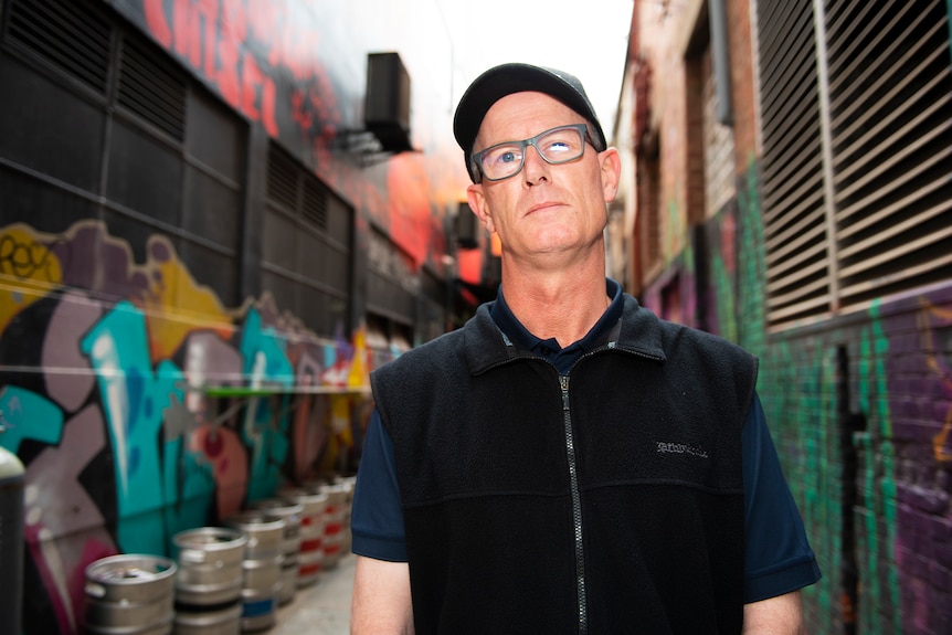 A man stands in an alleyway filled with graffiti