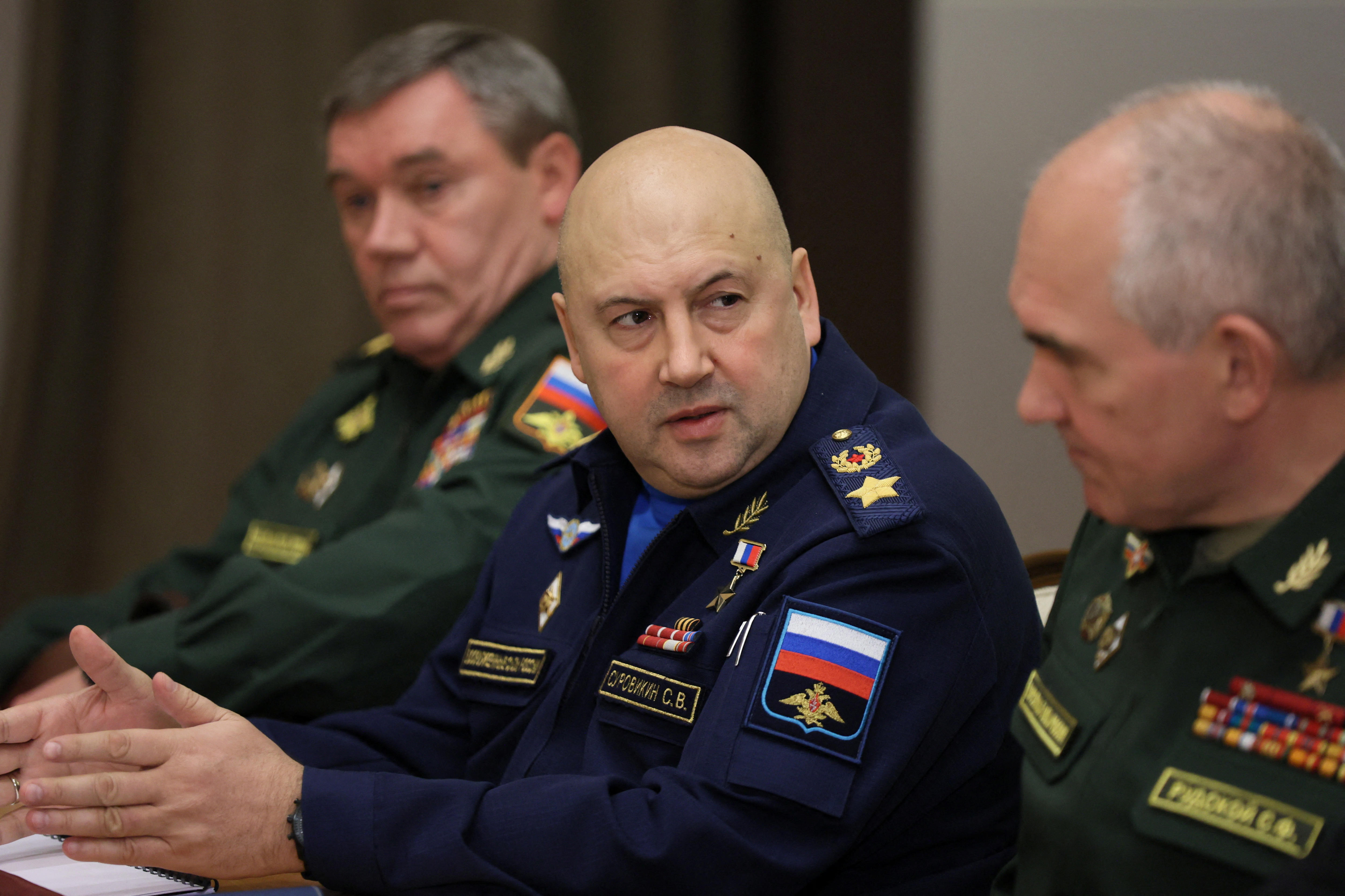 Sergei Surovikin, a bald man wearing a blue military uniform, gestures with his hands as he looks at a colleague