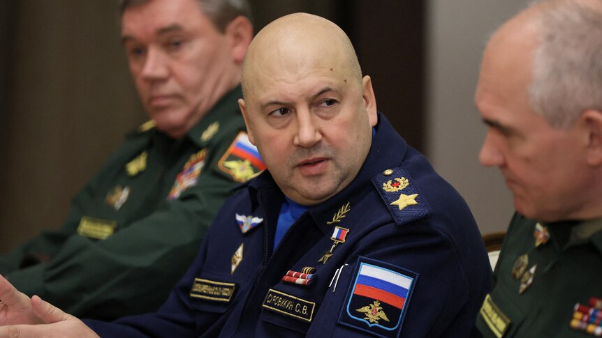 Sergei Surovikin, a bald man wearing a blue military uniform, gestures with his hands as he looks at a colleague