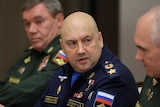 Sergei Surovikin, a bald man wearing a blue military uniform, gestures with his hands as he looks at a colleague