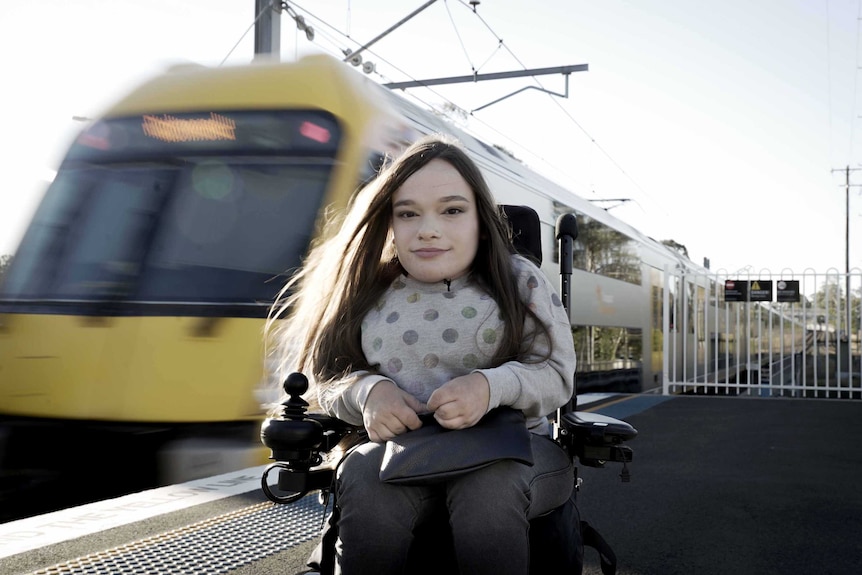 Jacqui Facaris, a 21-year-old woman who uses a wheelchair, waits on a platform as a train arrives