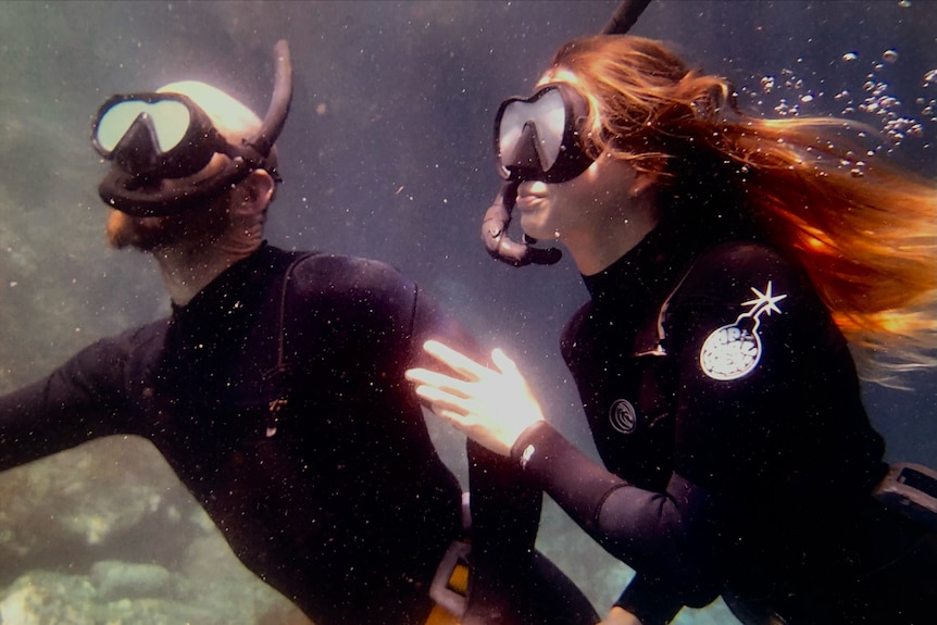 A male and female in black wetsuits with snorkel masks underwater