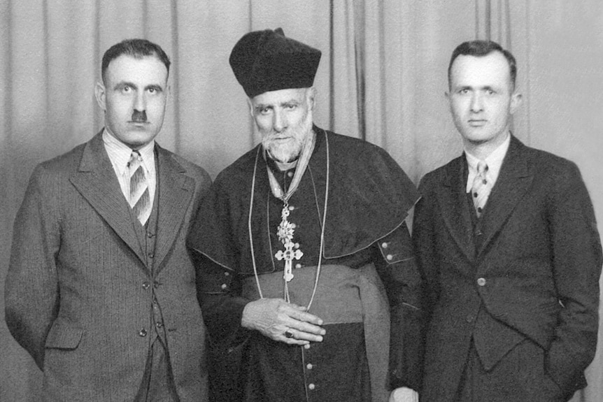 A black and white photo of three Lebanese men, with a Maronite priest, in his robes, in the middle.