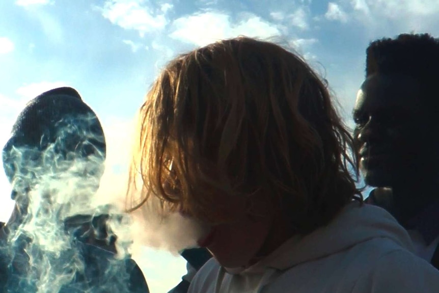 Teenagers stand around smoking marijuana through a bong.