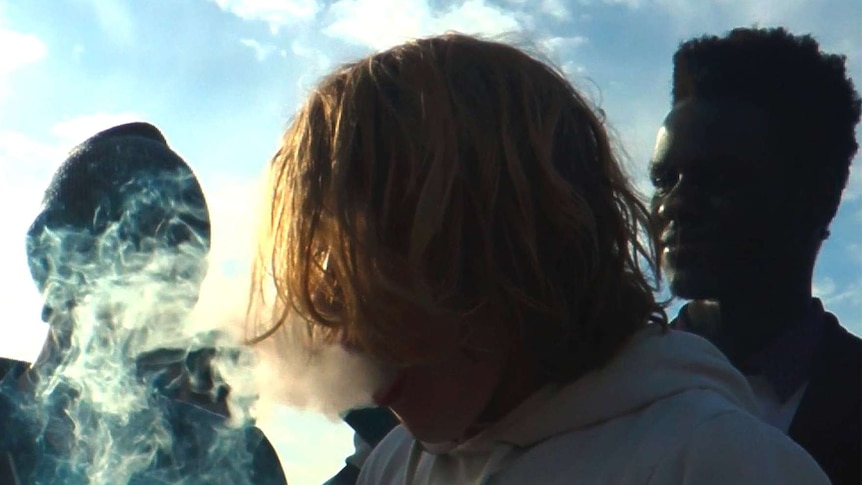 Teenagers stand around smoking marijuana through a bong.