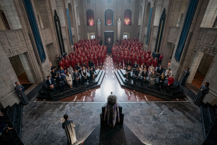 A grand room full of students in red, in a still from The Hunger Games