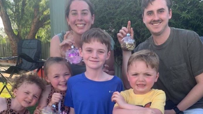 A woman and a man hold up Christmas baubles above four smiling children.