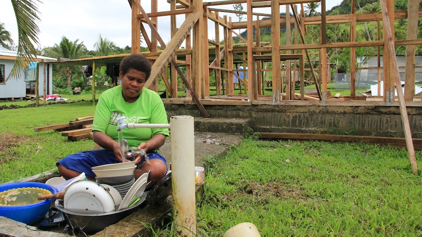 A woman washes her dishes in front of her partially rebuilt home in Narakoso village.