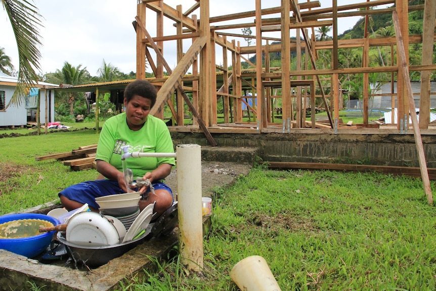 A woman washes her dishes in front of her partially rebuilt home in Narakoso village.