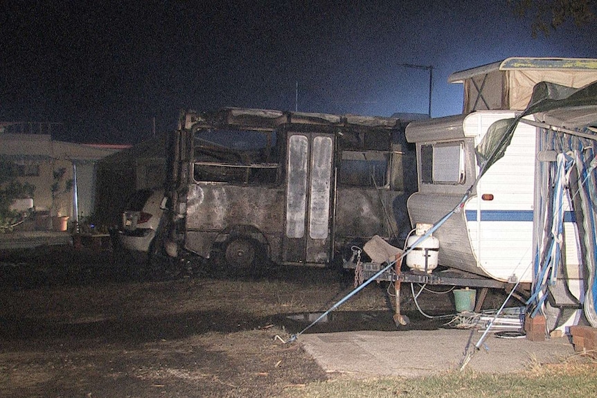 A burnt-out bus at Midland Tourist Park stands next to a caravan untouched by the blaze.