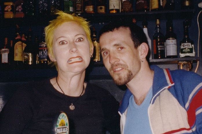 A woman and a man make funny faces for a camera as they stand behind a bar