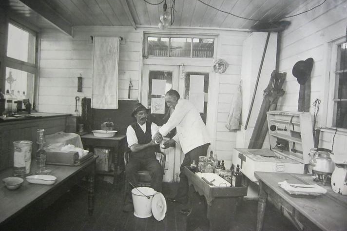 A black and white photos showing a man in a white coat bandaging another man's arm.
