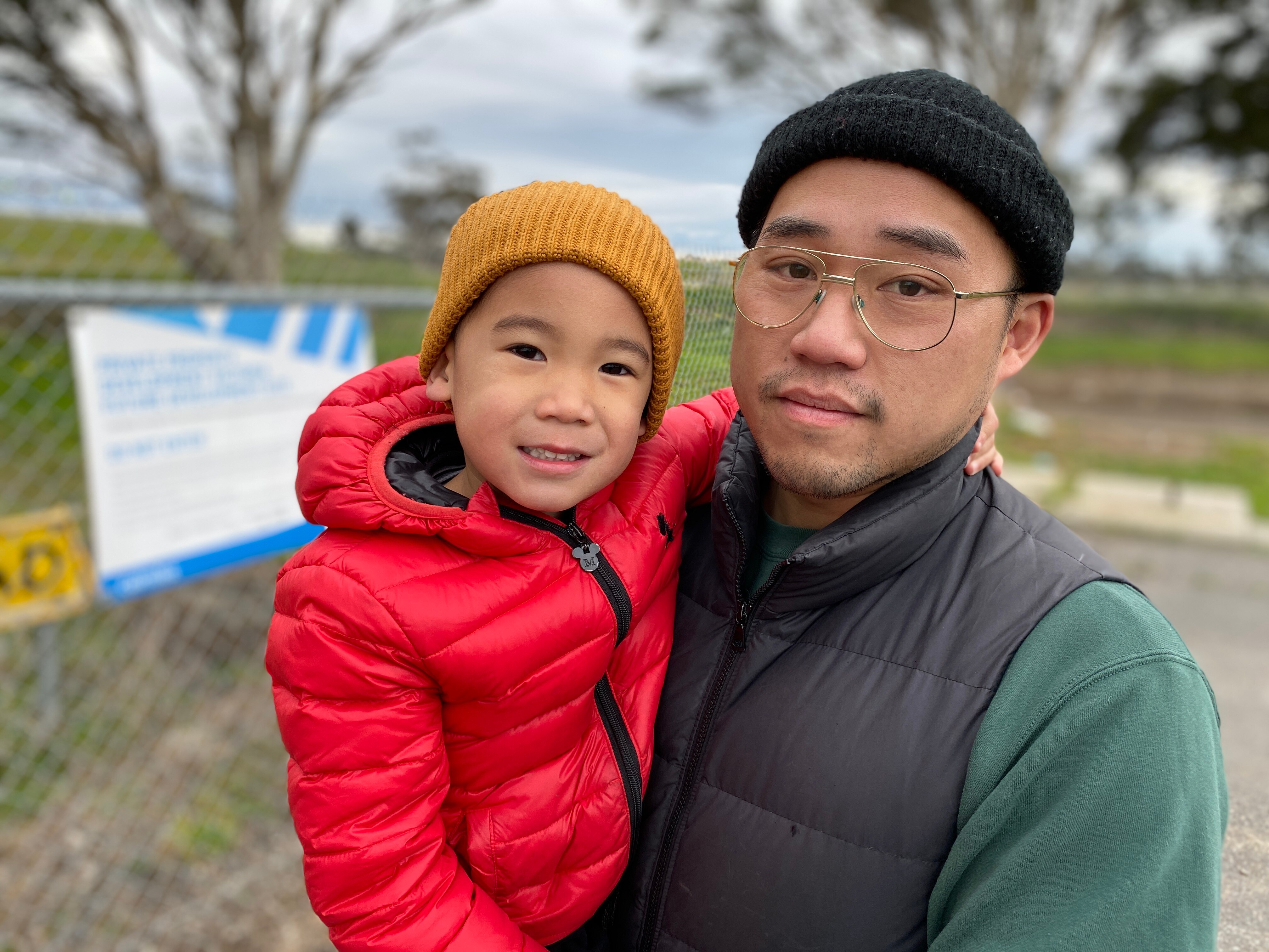 A man in spectacles and beanie holding a child