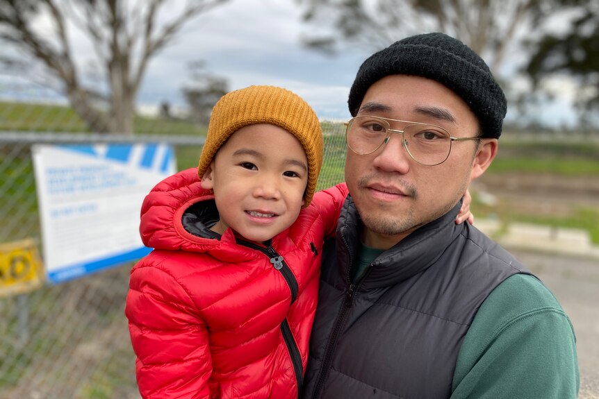 A man in spectacles and beanie holding a child