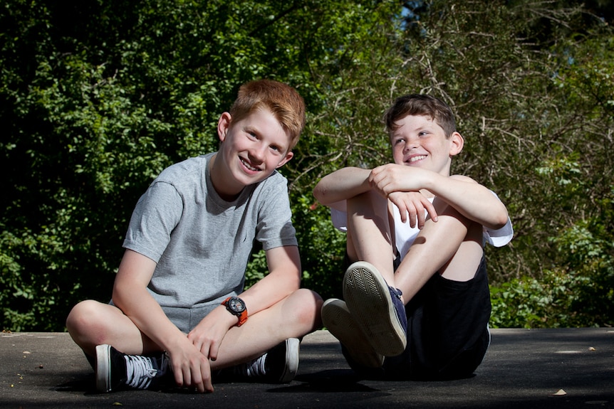 Two teen boys sitting on the ground, smiling.