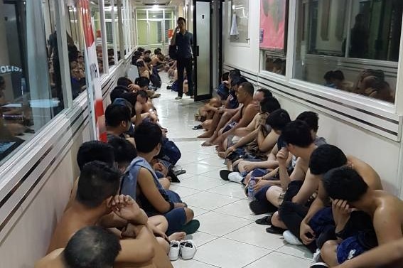 Men arrested during a raid on a North Jakarta gay club on May 2017 sit in a hall while a policeman watches them.