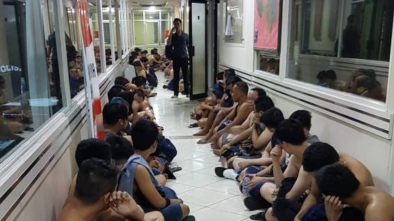 Men arrested during a raid on a North Jakarta gay club on May 21, 2017 sit in a hall while a policeman watches them.