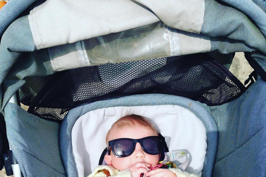 Baby Searyl looks up from their stroller while wearing sunglasses.