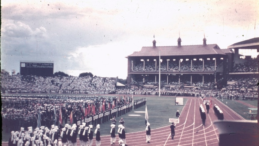 An old photograph slide of a ceremony on an athletics track at a busy stadium.