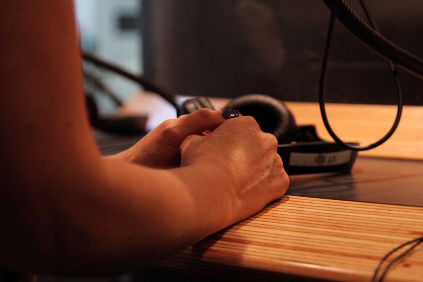 Emily's hands clasped on a desk near a set of headphones.
