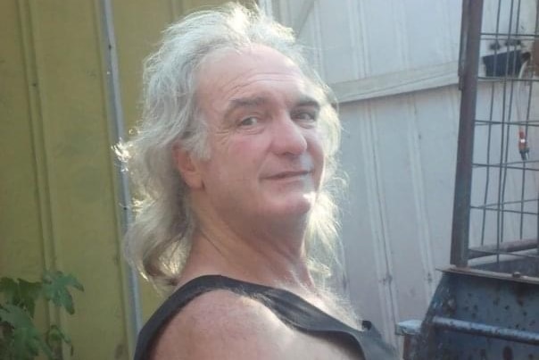 A man with medium length, grey hair smiles at the camera