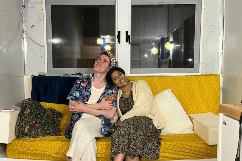 Two people in tropical attire smiling on a couch inside a tiny home
