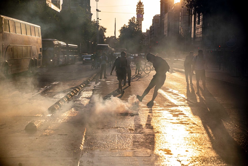With golden light filtering through smoke, a protester kicks a tear gas cannister on the streets